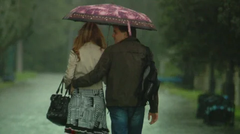 Man and a woman are walking under an umbrella in the rain in autumn Stock Footage