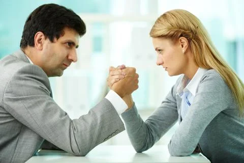 Man and woman in arm wrestling gesture on working table during meeting Stock Photos