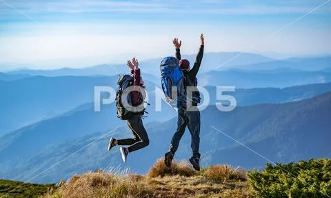 The man and a woman with backpacks jumping on the mountain Stock Photos