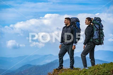 The man and a woman with backpacks standing on the mountain landscape backgro Stock Photos