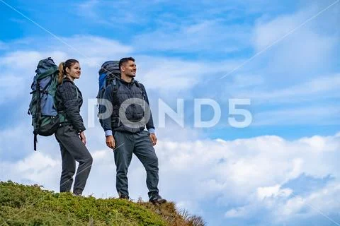 The man and a woman with backpacks standing on the mountain landscape backgro Stock Photos