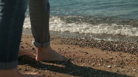 Man and woman with bare legs walking along seashore in summer day. Stock Footage