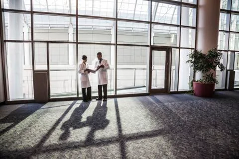 Man and woman doctors conferring over medical records in a hospital lobby. Stock Photos