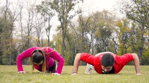Man and woman doing push-ups on the ground in the park slow motion Stock Footage 59798237