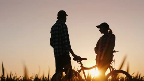 A man and a woman enjoy an evening walk at sunset, standing with a bicycle in Stock Footage 146324322