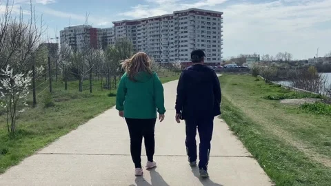 Man and woman go unhurriedly together along the walking path near the lake. Vídeo Stock