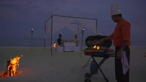 A man and woman have a bbq barbecue dinner on a tropical island beach. Stock Footage