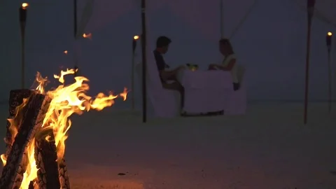 A man and woman have dinner on a tropical island beach with a campfire, slow mot Stock Footage