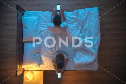 The man and woman hold a phone on the bed. evening night time. view from abov Stock Photos