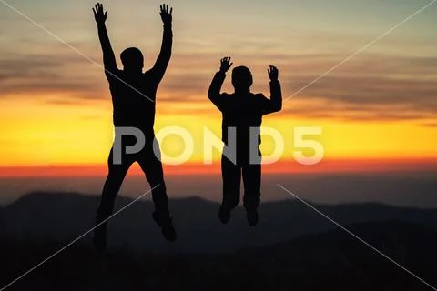 The man and a woman jumping on the mountain on the sunset background Stock Photos
