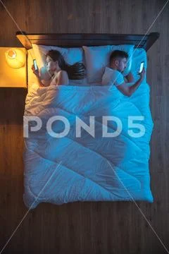 The man and woman phone on the bed. evening night time. view from above Stock Photos