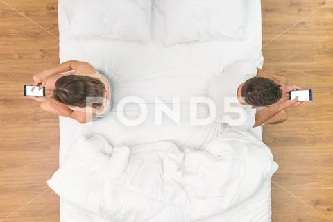 The man and woman with phone sit on the bed. view from above Stock Photos