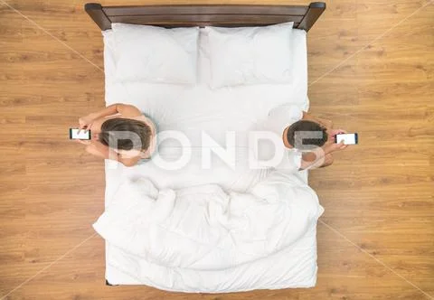 The man and woman with phone sit on the bed. view from above Stock Photos