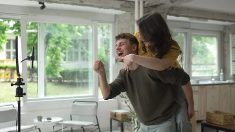 Man and woman piggy back while record video and show keys of new home Video stock 312791663
