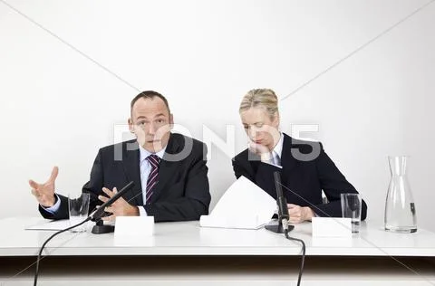 A man and a woman sitting at a desk with microphones and documents Stock Photos