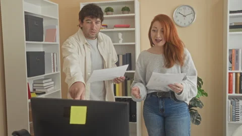 Man and woman standing by computer, holding documents and pointing with han.. Stock Footage 337391780