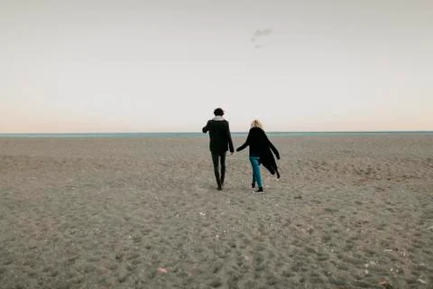 Man and woman walking by the beach sand at sunset. Stock Photos