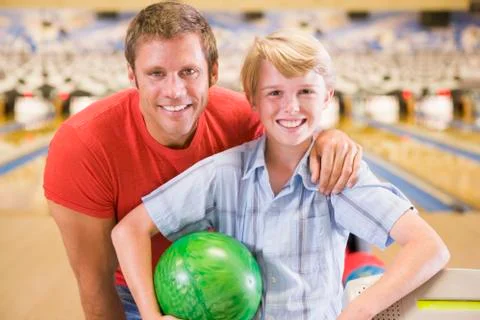 Man and young boy in bowling alley holding ball and smiling Stock Photos