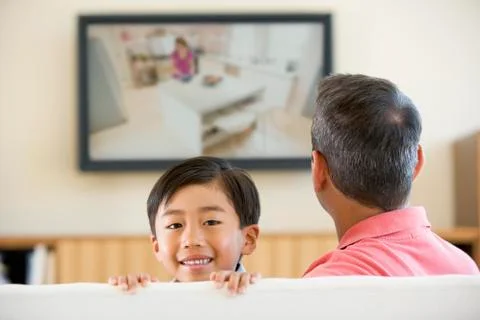 Man and young boy in living room with flat screen television smiling Stock Photos