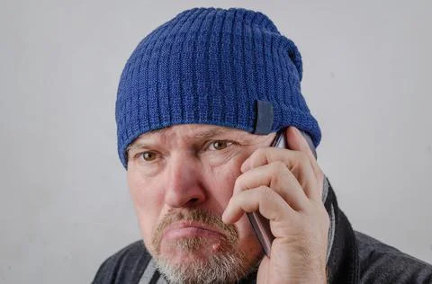 A man is angry while talking on his cell phone. Person wearing a blue hat aga Stock Photos