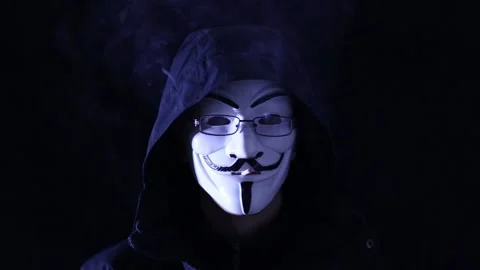 A man in an anonymous mask smokes a cigarette on a black background Stock Footage 169650759