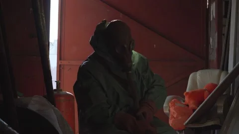 Man in antinuclear clothing changes gasmask filter indoor. Stock Footage 232940439