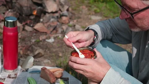 A man with appetite eats canned fish in tomato sauce with a fork. Outdoor picnic Stock Footage 160341014
