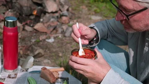 A man with appetite eats canned fish in tomato sauce with a fork. Outdoor picnic Stock Footage 160944641