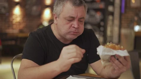 A man with appetite eats a hamburger in a fast food restaurant. Stock Footage 146063507