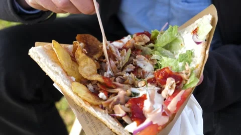 A man appetizingly holds and eats a kebab in a bread pita filled with chicken Stock Footage 304998612