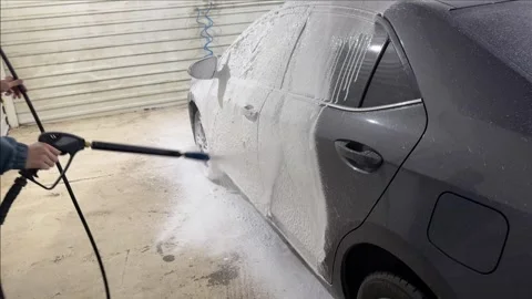 A man applies a cleaning solution with a high pressure cleaner at a car wash Stock Footage 308818777