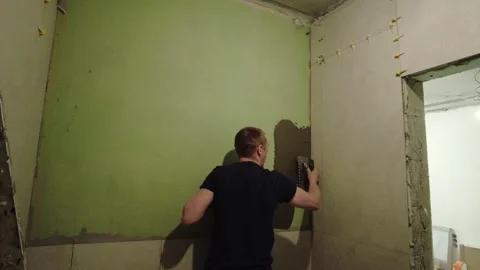 Man applies plaster to a green wall inside a room during home renovation work in Stock-Footage 332479103