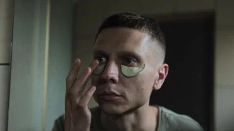 Man applying cucumber slices under his eyes for a refreshing skincare routine. Stock Footage 307787113