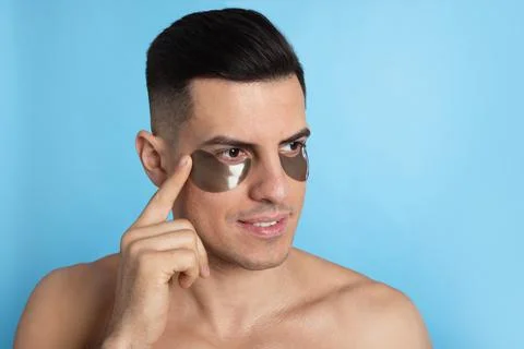 Man applying dark under eye patch on light blue background. Space for text Stock Photos