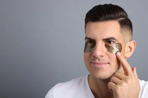 Man applying dark under eye patch on grey background. Space for text Stock Photos