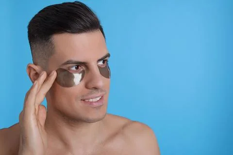 Man applying dark under eye patch on light blue background. Space for text Stock Photos