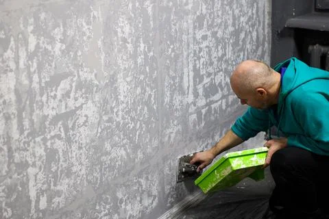 Man applying decorative plaster on wall in apartment using trowel, craft. Stock Photos
