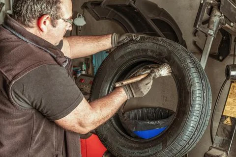 Man applying lubricant to a tyre using a brush in a garage Stock Photos