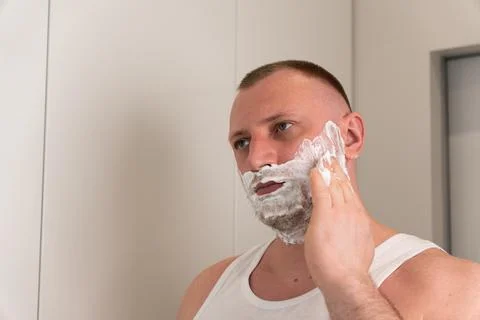 Man applying shaving foam on face before grooming routine Stock Photos