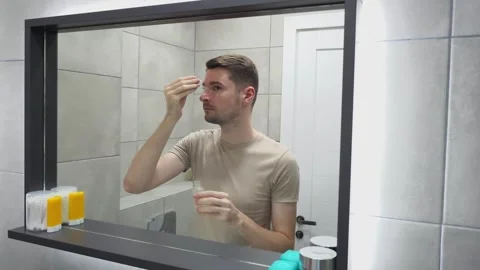 Man applying skin serum in front of a bathroom mirror. Hygiene and skincare Stock Footage 283931812