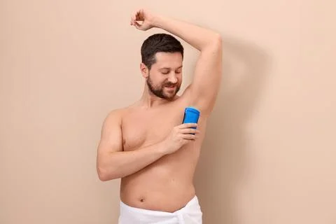 Man applying solid deodorant on beige background Stockfoto's