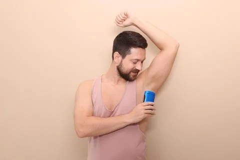 Man applying solid deodorant on beige background Stockfoto's