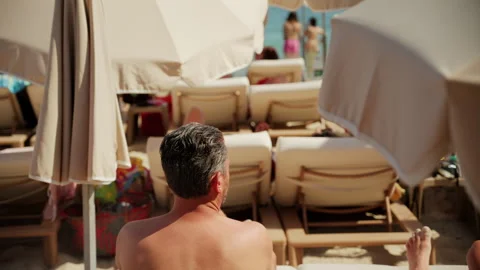 Man applying a spray sunscreen on his face at the beach surrounded by big Stock Footage 337011062
