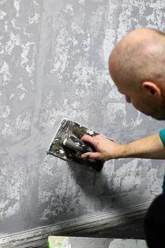 Man applying textured plaster to wall with a trowel. Stock Photos