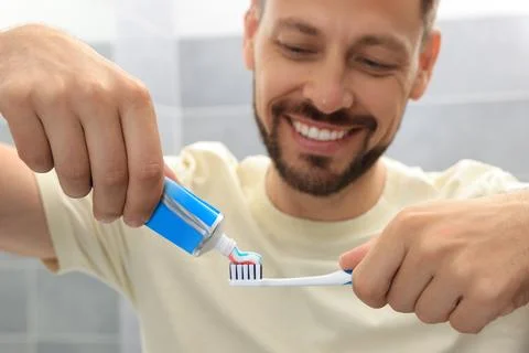 Man applying toothpaste onto brush in bathroom, focus on hands Stock Photos