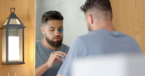 Man applying under eye patch in bathroom, focusing on skincare routine Vídeos de archivo 297930771