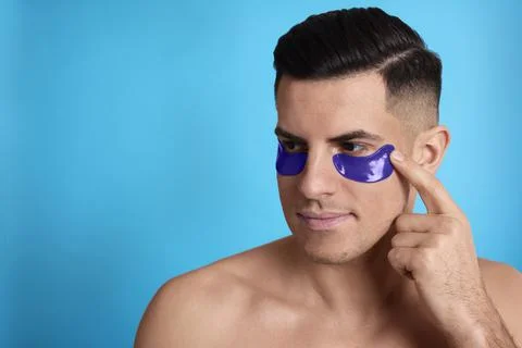 Man applying under eye patch on light blue background. Space for text Stock Photos