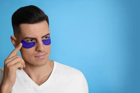 Man applying under eye patch on light blue background. Space for text Stock Photos