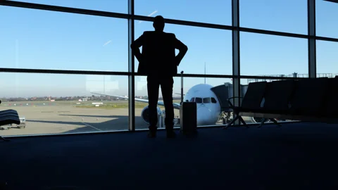 Man approach terminal window, stands and looks out to parked airliner Video stock 320118062