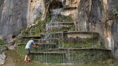 A man approaches an artificial cascading waterfall in a rock and washed Stock Footage 91810083